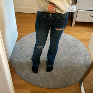 Blå bootcut jeans med slitningar - Säljer ett par snygga blå jeans med bootcut-modell och slitna detaljer på knäna. Sitter väldigt lågmidjat. Säljer för att de tyvärr är för små. 