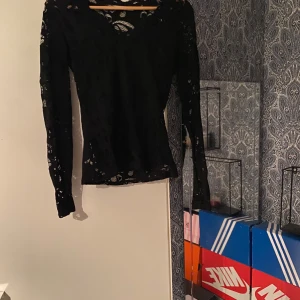 Svart spetsblus med v-ringning - Säljer en svart långärmad blus i spets med v-ringad hals. Toppens genombrutna spets ger en snygg och trendig look, perfekt att styla med jeans eller kjol. Figurnära passform och transparenta detaljer gör den extra cool.