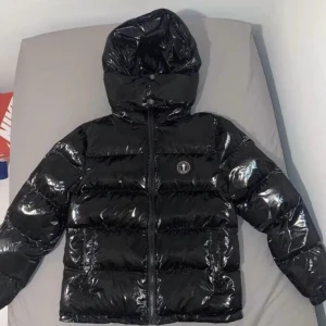 Svart pufferjacka från Trapstar - Säljer en glansig svart pufferjacka från Trapstar med huva och dragkedja. Jackan har tydlig logga på bröstet och stor Trapstar-text på ryggen. Perfekt för kalla dagar och riktigt street. Jackan är vadderad och har en modern look.