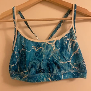 Blå mönstrad bikinitopp från Funkita - Säljer en blå och vit bikini topp från Funkita med coolt marmorerat mönster. Toppen har smala axelband som korsas i ryggen och är tillverkad i 100% polyester. Perfekt för träning eller bad och ger en sportig vibe.