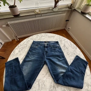 Blå Replay jeans Sandot relaxed tapered - Snygga blå jeans från Replay, modell Sandot med relaxed tapered passform. Klassisk femficksdesign, ljus tvätt och diskreta slitningar. Märkespatch i läder baktill och detaljerade bakfickor. De är aldrig använda men gick inte att lämna tillbaks. I storlek L 30 och W 32