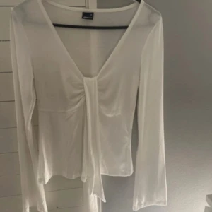 Vit omlottopp från Gina Tricot - Snygg vit omlottopp från Gina Tricot i tunn och lätt polyester. Toppen har lång ärm, v-ringning och knyt framtill. Strl XS