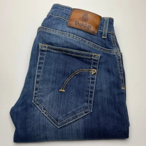 Dondup jeans  - Snygga blå jeans från Dondup med klassisk femficksdesign och kontrastsömmar. Jeansen har en läderpatch med logga bak i midjan och är tillverkade i mjukt bomullsmaterial. Perfekta för en avslappnad och stilren look.