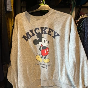 Grå Mickey Mouse sweatshirt - Säljer en grå sweatshirt med stort tryck av Mickey Mouse och texten 'The True Original EST 1928' framtill. Tröjan har rund hals och långa ärmar, perfekt för dig som gillar retro och Disney-vibes.