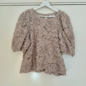  Spets blus  - Superfin beige blus från Lindex med 3D-blommor över hela tyget. Blusen har trekvarts ärm, rund hals och en liten knapp i nacken. Den är sparsamt använd och har inga skavanker💞💞