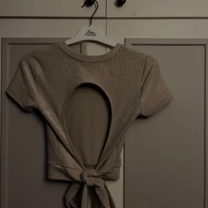 Beige ribbad topp, öppen rygg  - Supersnygg beige ribbad topp från Gina Tricot i croppad modell. Toppen har korta ärmar, rund halsringning och en öppen rygg med knytband nedtill. ❤️❤️