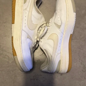 Nike Air vita sneakers - Fräscha Nike Air Force 1 sneakers i helvitt med klassisk design och låg profil. Skorna har snörning, rund tå och platt sula med gummidetaljer. Tillverkade i skinn och syntetmaterial, med ikonisk swoosh på sidorna. Perfekt för dig som gillar clean och tidlös stil.