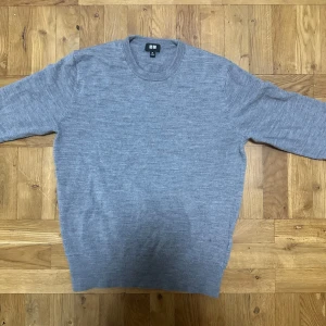 Grå merinoulltröja från Uniqlo XS - Säljer en stilren grå tröja från Uniqlo i mjuk merinoull. Klassisk rund halsringning och långärmad modell som passar perfekt till lager-på-lager. Enkel och clean look som funkar till det mesta. Perfekt för dig som gillar minimalistisk stil.