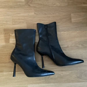 Svarta stövletter med klack - Snygga svarta stövletter i skinn med spetsig tå och hög smal klack. Dragkedja på insidan för enkel påtagning. Perfekta för dig som vill ha en stilren och edgy look.