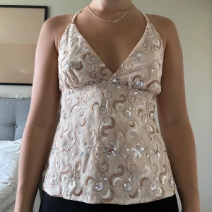 Guldig/beige topp  - Snygg beige topp med guldiga och glittriga detaljer. Toppen är helt öppen i ryggen och knyts på två ställen. Använd en gång, fint skick. Tryck inte på KÖP DIREKT utan skriv privat om du är intresserad! 💛