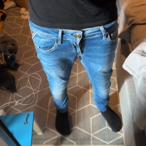 Replay slim blå jeans herr - Säljer ett par snygga Replay  jeans i klassisk blå tvätt med coola slitningar och detaljerade sömmar på bakfickan. Modellen har smal passform och normal midja, perfekt för dig som gillar en modern och stilren look. Jeansmaterialet är mjukt och följsamt.