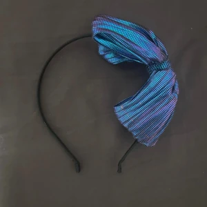 Diadem med en stor rosett - Svart diadem med en stor rosett i blått och lila. Rosetten har ett rutigt mönster och skimrar i ljuset