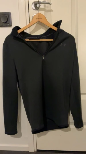 Svart Under Armour half zip tröja - Hej! Svart långärmad tröja från Under Armour med half zip och ståkrage. Modellen är loose fit och tillverkad i ett mjukt syntetmaterial som andas. Perfekt för träning eller när du vill ha en sportig look. Diskret logga på bröstet och axlar med ribbad detalj.