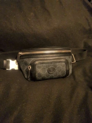 Gucci väska svart - Äkta svart Gucci väska i i topp skick. Gucci Aria samling, bälteväska från Gucci med GG canvas och en fräsch gucci logga på framsidan. Väskan har 3 stycken fickor 2 fram och 1 diskret bakom.