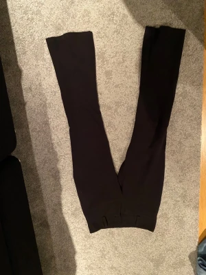 Svarta bootcut kostymbyxor Gina Tricot - Svarta kostymbyxor från Gina Tricot i storlek S. Byxorna har bootcut-ben, låg midja och två bakfickor med lock och knapp. Snygga bälteshällor och klassisk rak passform. Perfekta för dig som gillar stilrena och tidlösa plagg.