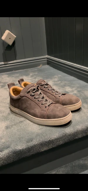 Loubutins  - Snygga gråa sneakers från Paris i mjuk mocka med beige innersida och vit platt sula. Skorna har rund tå och klassisk snörning framtill. Perfekt för dig som gillar stilrena och neutrala färger med en touch av lyxig känsla. Storlek 44