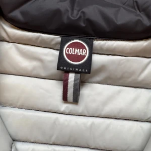 Svart pufferjacka från Colmar, stl 48 - Snygg svart pufferjacka från Colmar Originals med quiltad design och dragkedja framtill. Jackan har en stilren look med diskret logga på bröstet och ljusgrå insida. Perfekt för dig som vill ha en lätt och trendig jacka till höst och vinter.