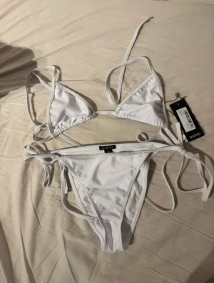 Vit bikini med knyt  - Snygg vit bikini med klassisk trekants-bh och knyt i sidorna på både över- och underdel. Helt nya!!
