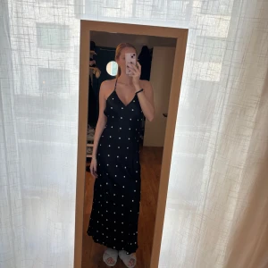 Svart prickig långklänning med öppen rygg - Öppen i ryggen och lång i passformen, är 175cm på bilden. Helt ny med prislapp. Storlek M. 