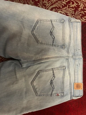 Ljusblå Replay jeans straight fit - Säljer ett par ljusblå jeans från Replay 28/32  med klassisk femficksdesign och raka ben. Jeansen har snygga detaljer på bakfickorna och en läderpatch med Replay-logga i midjan. Har inte blivit använda mer än en gång 