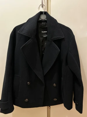 Mörkblå kappa - Säljer en mörkblå kappa  från Pull&Bear med klassisk dubbelknäppning och breda slag. Jackan har två framfickor och är tillverkad i ullblandning som ger en snygg och stilren look. 