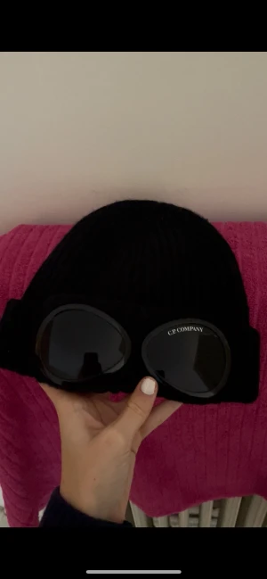 C.P. COMPANY mössa  - Svart stickad mössa från C.P. Company, klassisk modell med uppvikt kant och tydlig logga på glasögonen. Använd flertal gånger men fortfarande i bra skick! Köpt på NK, taggen går att scanna 💓Nypris var 1200 men säljer för 400 pga att den har lite färg på insidan men den syns inte när man har på sig den och den inte är min stil längre och vill bli av med den👍skriv om ni har några frågor!