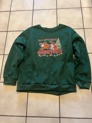 Grön jultröja med tryck - Mörkgrön sweatshirt med julmotiv och texten 'On a joyful night Christmas' framtill. Trycket har tomte, pepparkaksgubbe, julgran och färgglada detaljer. Tröjan har rund hals och är tillverkad i mjuk polyester. Perfekt för dig som vill maxa julkänslan!