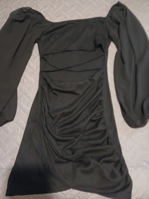 Svart kort klänning från SHEIN - Supersnygg svart klänning från SHEIN i storlek XS. Modellen är kort med puffiga långärmar och har en offshoulder-design. Materialet är mjukt och stretchigt, troligen polyester. Klänningen har snygga draperingar framtill som ger en cool look.