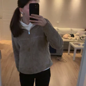 Beige teddyjacka med dragkedja - Mjuk och fluffig beige teddyjacka med hel dragkedja framtill. Jackan har en enkel, rundad form och långärmade ärmar. Perfekt för att hålla sig varm och samtidigt se soft ut.