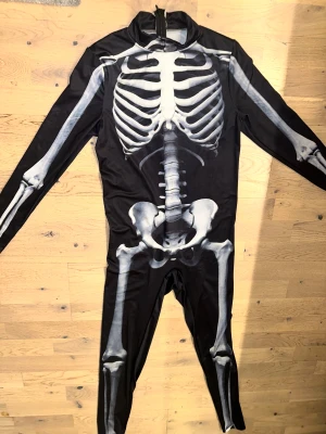 Svart skelettdräkt med dragkedja Svart overall halloween dräkt - Cool helkroppsdräkt med skelettmotiv i vitt och grått på svart bakgrund. Dräkten har lång ärm och ben, samt en dragkedja i nacken för enkel påklädning. Materialet är mjukt och stretchigt, perfekt för halloween eller temafest.Svart helkroppsdräkt med ett skelett tryckt på fram- och baksidan. Dräkten har långa ärmar och ben, samt en dragkedja framtill. Storlek S/M stretch material super bra! 👍🏻 använd en gång inköpt för 39€. 👻 🎃 