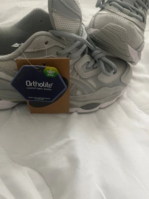 Asics  Skor  - Snygga grå ASICS sneakers med Ortholite komfortsula. Skorna har mesh och syntetpaneler, snörning och en platt, mönstrad sula för extra grepp. Perfekt för dig som gillar sportig stil och vill ha bekväma skor med cool design.