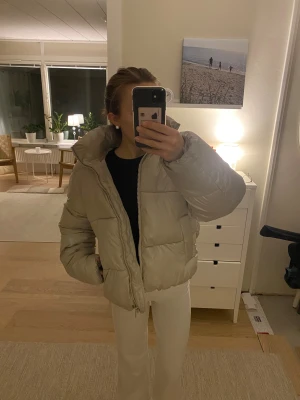 Beige pufferjacka från H&M - Säljer en beige pufferjacka från H&M i storlek S. Jackan har en hög krage, huva och dragkedja framtill. Perfekt för kalla dagar, super snygg!!😍🙌🏼