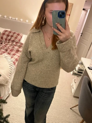 Beige stickad tröja med krage från H&M - Mysig beige stickad tröja från H&M i storlek S. Tröjan har en bred krage och v-ringad hals, samt långa ärmar med ribbade muddar. Perfekt för lager-på-lager och chill dagar. Materialet är mjukt och ger en avslappnad vibe.
