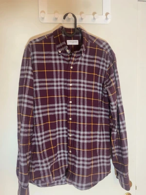 Rutig flanelskjorta från John Henric - Säljer en snygg rutig flanelskjorta från John Henric i mörklila och grått med tunna gula linjer. Skjortan har klassisk krage, långa ärmar och knappar framtill. Perfekt för dig som gillar stilrena och coola mönster.