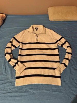 Randig half zip tröja från H&M - Säljer en vit stickad tröja från H&M med svarta horisontella ränder och half zip-dragkedja vid kragen. Tröjan har långärmad design och är ribbad i materialet, vilket ger en snygg och modern look. Perfekt för dig som gillar klassiska mönster och bekväma plagg. Priset går alltid att diskutera 
