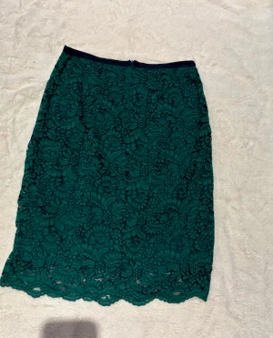 Grön spetskjol från NAF NAF - Säljer en snygg grön kjol från NAF NAF med vacker spets och rak passform. Kjolen har en dold dragkedja bak och är fodrad för extra komfort. Perfekt att matcha med en enkel topp och boots. Spetsdetaljerna ger en elegant vibe.