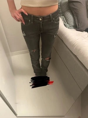 Grå jeans med slitningar och broderi - Säljer ett par grå jeans med hål som jag klippt själv samh slitningar. Modellen har låg midja och raka ben. Jeansen är tillverkade i denim och har vita kontrastsömmar för extra edge. 