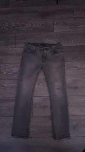  Nudie Jeans - Säljer ett par gråa skinny jeans från Nudie Jeans i storlek W32 L30. Jeansen har klassisk femficksdesign, svarta sömmar och Nudie-logga på bakfickan. Materialet är stretchigt jeans och passformen är tight med smal siluett.