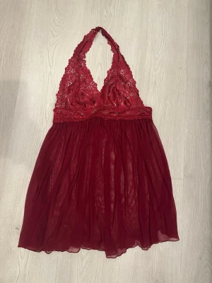 Vinröd spetsklänning  - Säljer en vinröd spetsklänning och djup v-ringning. Överdelen är dekorerad med blommig spets och har tunna axelband. Nederdelen är gjord i ett skirt, lätt material som ger ett luftigt intryck.