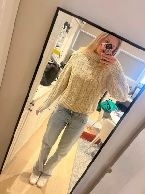 Beige stickad polotröja med flätmönster - Säljer en beige stickad polotröja med grovt flätmönster och ribbad krage. Tröjan har en loose passform och långa ärmar, perfekt för att hålla sig varm under kyliga dagar. Supermysig och trendig att styla med jeans eller kjol.