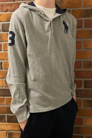 Polo Ralph Lauren Hoodie - Grå hoodie från Ralph Lauren med mörkblå polospelare broderad på bröstet och en stor 3:a på ärmen. Storleken är XL i barn. Typ som xs i vuxen storlek. 