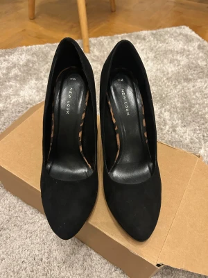 Svarta plateaupumps från New Look - Säljer ett par svarta pumps från New Look med hög klack och platåsula. Skorna har spetsig tå och är klädda i mockaliknande material. . Boxen medföljer 