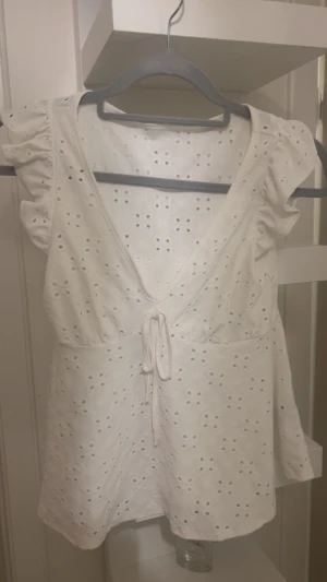 Vit blus med knyt  - Supersöt vit blus från SHEIN i storlek XS. Blusen har broderade hålmönster, volangärmar och djup v-ringning med knyt framtill. Skriv gärna för fler bilder eller frågor💗