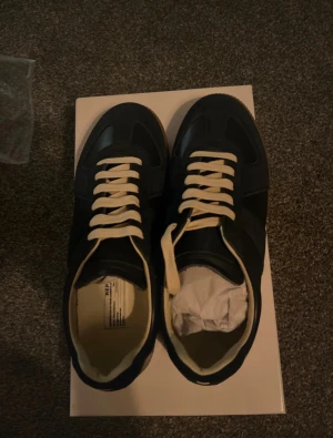 Maison Margiela gats - Maison Margiela sneakers i navy blue med kontrasterande vita snören och beige insida. Klassisk rund tå och platt sula. Snygg retrostil med stilrena paneler och detaljer. Kommer i originalkartong. Perfekt för dig som gillar exklusiva och tidlösa sneakers. 