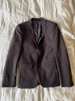 Svart kavaj från Lindbergh White - Stilren svart kavaj från Lindbergh White i storlek EU 42. Kavajen har klassisk passform, enkla knappar framtill och fickor med lock. Tillverkad i 100% polyester med snyggt foder och diskreta detaljer vid ärmslutet.