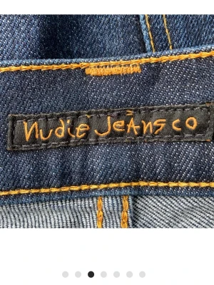 Nudie Jeans - Snygga mörkblå jeans från Nudie Jeans med klassisk femficksdesign och kontrastsömmar i orange. Modellen har en rak passform med lätt bootcut och är tillverkad i slitstarkt denimtyg av bomull. Perfekt för dig som gillar stilrena och tidlösa jeans.