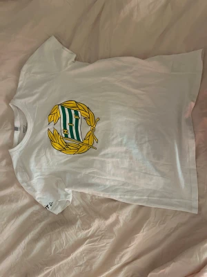 Vit Hammarby t-shirt med tryck - Säljer en vit t-shirt från Craft med Hammarby IF:s emblem i grönt, gult och vitt på bröstet. T-shirten har korta ärmar och rund hals. Aldrig använd Materialet är mjuk bomull som känns skönt mot huden. 