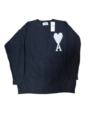 Ami Paris svart stickad tröja - Svart stickad tröja från Ami med rund halsringning och ribbade muddar. På bröstet finns ett vitt hjärta och bokstaven A som ger en unik touch. Perfekt för dig som gillar stilrena plagg med en twist.