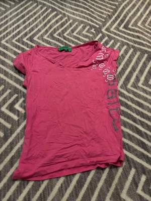 Rosa v-ringad t-shirt med tryck - Säljer en rosa t-shirt med v-ringning och coolt tryck i vitt och grönt på ena axeln och sidan. T-shirten är kortärmad och i mjuk bomull. Storleken är M, men den passar mig väldigt bra som S. Tröjan är också lite cropped.