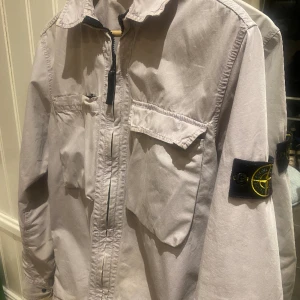 Stone Island Overshirt - Säljer nu denna feta stone island Overshirten. Den är i bra skick och har inga defekter, 9/10. Färgen är vit och lite svagt lila. Självklart är den äkta. Kom dm om ni har några frågor!